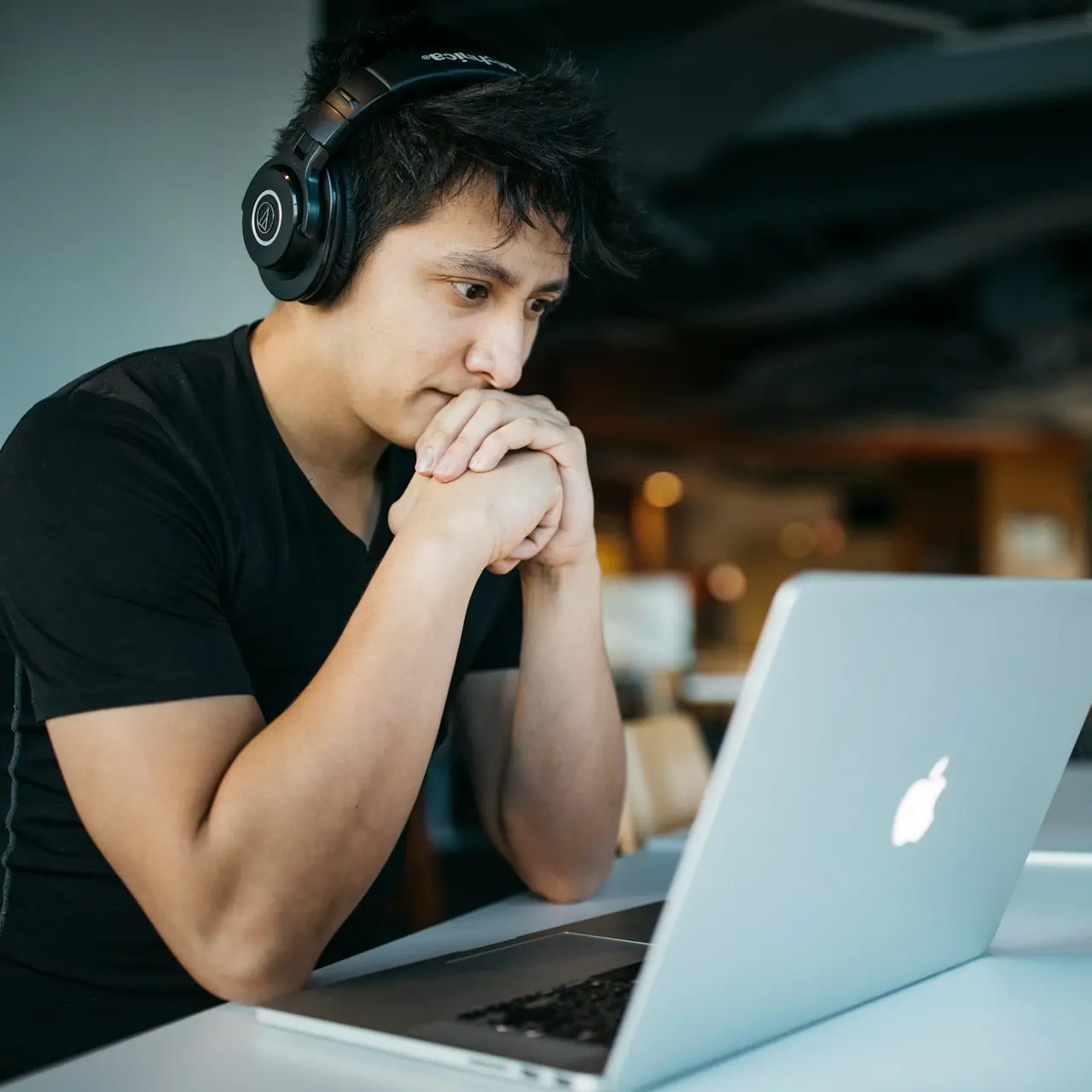 man wearing headphones while sitting on chair in front of MacBook